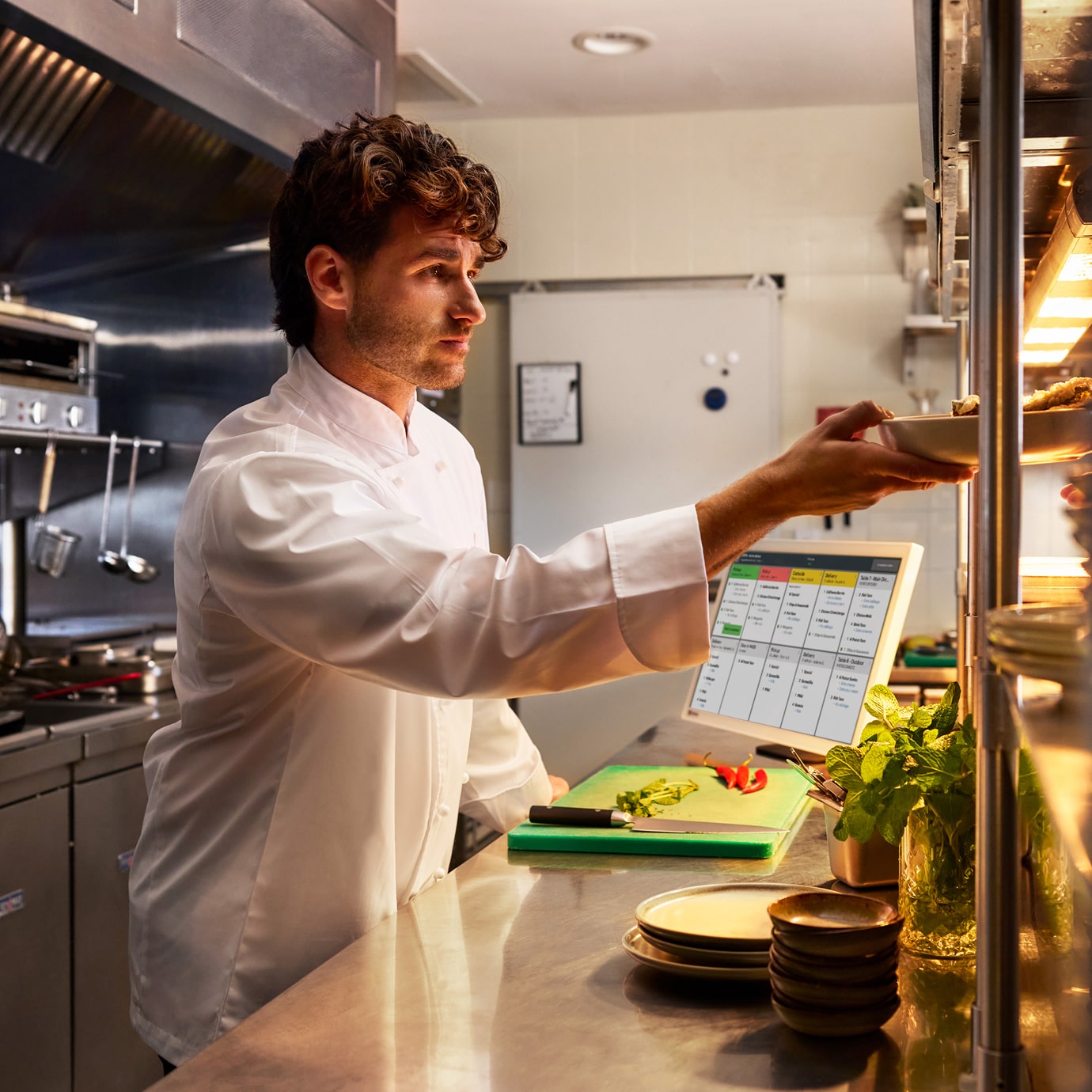 Chef placing a plated dish on a service shelf next to a KDS